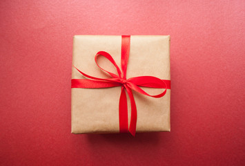 Gift box wrapped in brown colored craft paper and tied with red bow on dark red background.