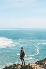 A man tourist with a backpack stands in solitude at Cape Roca in Portugal and enjoys a beautiful view of the Atlantic Ocean.