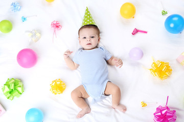 Cute baby with birthday decorations lying on white bed