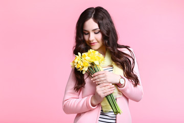 Beautiful woman in fashion clothes with narcissus flowers on pink background