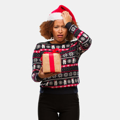 Young black woman holding a gift in christmas day tired and very sleepy