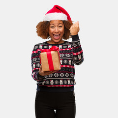 Young black woman holding a gift in christmas day screaming very angry and aggressive