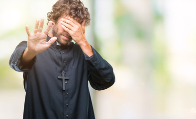 Handsome hispanic catholic priest man over isolated background covering eyes with hands and doing stop gesture with sad and fear expression. Embarrassed and negative concept.