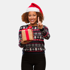 Young black woman holding a gift in christmas day showing number one