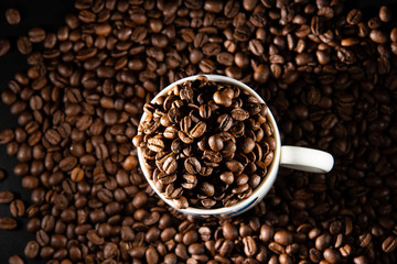 white cups with a pattern and grains of coffee on a black background