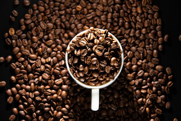 white cups with a pattern and grains of coffee on a black background