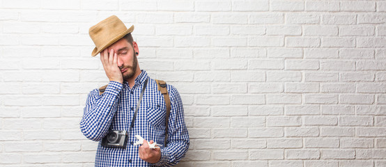 Young traveler man wearing backpack and a vintage camera worried and overwhelmed, forgetful, realize something, expression of shock at having made a mistake. Holding a airplane model.