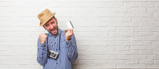 Young traveler man wearing backpack and a vintage camera very happy and excited, raising arms, celebrating a victory or success, winning the lottery. Holding a credit card.