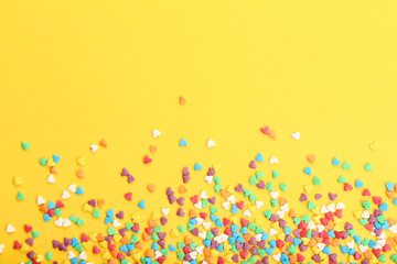 Colorful heart shaped sprinkles on yellow background