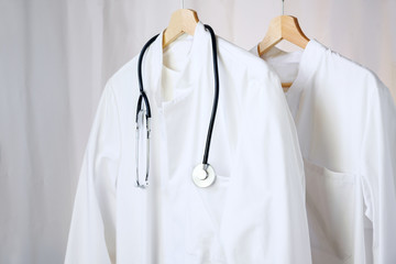 white medical doctor or physician lab coats with stethoscope hanging on clothes hangers, copy space