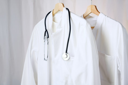 White Medical Doctor Or Physician Lab Coats With Stethoscope Hanging On Clothes Hangers, Copy Space