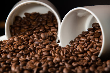 white cups with a pattern and grains of coffee on a black background