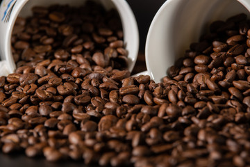 white cups with a pattern and grains of coffee on a black background