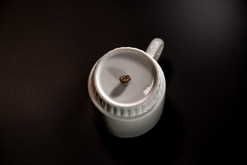 white cups with a pattern and grains of coffee on a black background
