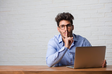 Young business man sitting and working on a laptop keeping a secret or asking for silence, serious face, obedience concept