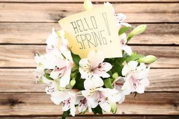 Bouquet of alstroemeria flowers with text Hello Spring on wooden background