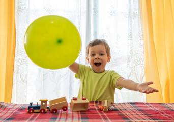 joyful boy playing with a wooden train and a balloon