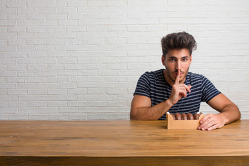 Fototapeta premium Young handsome and natural man sitting on a table keeping a secret or asking for silence, serious face, obedience concept. Eating chocolate doughnuts.