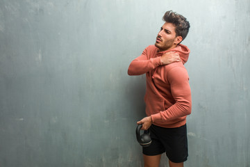 Young fitness man against a grunge wall with back pain due to work stress, tired and astute. Holding an iron dumbbell.