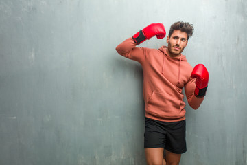 Young fitness man against a grunge wall making a suicide gesture, feeling sad and scared forming a gun with fingers.