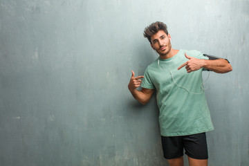 Young fitness man against a grunge wall proud and confident, pointing fingers, example to follow, concept of satisfaction, arrogance and health. Wearing an armband with phone.