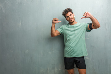 Young fitness man against a grunge wall proud and confident, pointing fingers, example to follow, concept of satisfaction, arrogance and health. Wearing an armband with phone.