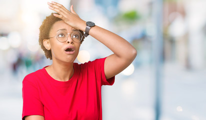 Beautiful young african american woman wearing glasses over isolated background surprised with hand...