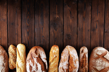 Assortment of baked bread and bread rolls on wooden table background