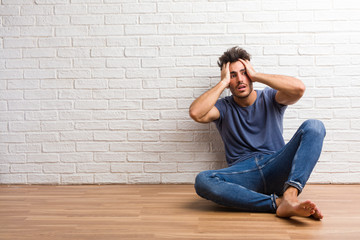 Young natural man sit on a wooden floor frustrated and desperate, angry and sad with hands on head