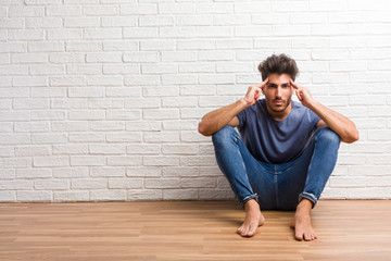 Young natural man sit on a wooden floor man making a concentration gesture, looking straight ahead focused on a goal
