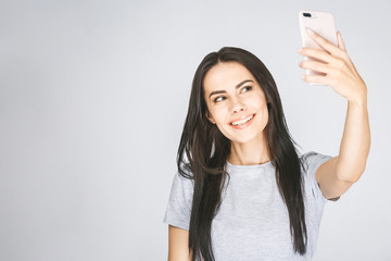 Studio portrait of beautiful woman smiling with white teeth and making selfie, photographing herself over white background.