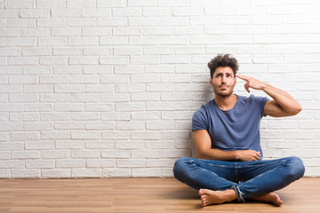 Young natural man sit on a wooden floor making a suicide gesture, feeling sad and scared forming a gun with fingers