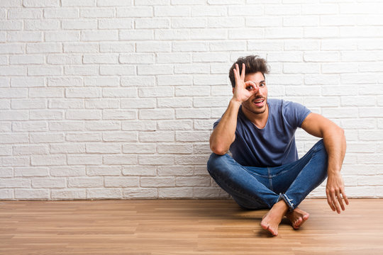 Young natural man sit on a wooden floor cheerful and confident doing ok gesture, excited and screaming, concept of approval and success - Powered by Adobe