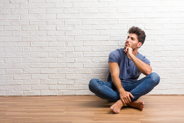 Young natural man sit on a wooden floor thinking and looking up, confused about an idea, would be trying to find a solution