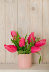 Spring bouquet of pink tulips with branches of a blossoming tree on a light wooden background.