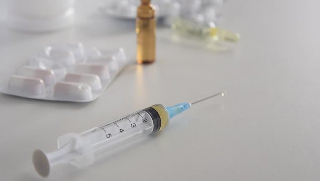 Medical syringe with injection solution, medicine pills and capsules on white background. Healthy medical concept