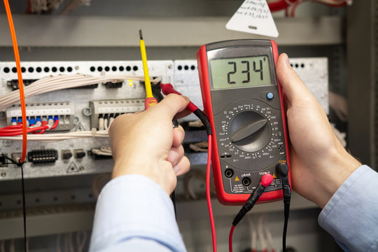 Electrician adjusts electrical control panel on power station, using tester.