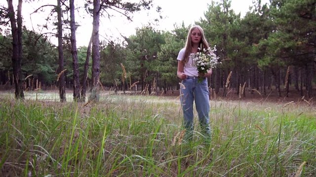 Tender young woman picking wild flowers composing aesthetic bouquet in forest nature slow motion landscape