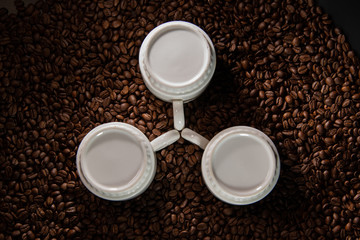 white cups with a pattern and grains of coffee on a black background