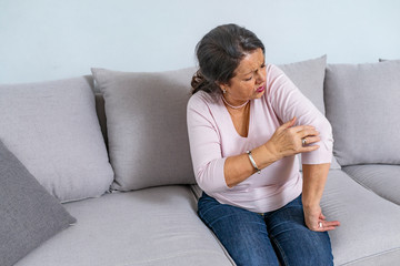 Fototapeta premium Elbow Pain In An Elderly Person. People, health care and problem concept - unhappy woman suffering. Senior woman suffering from pain in hand at home. Mature woman suffering from elbow pain at home