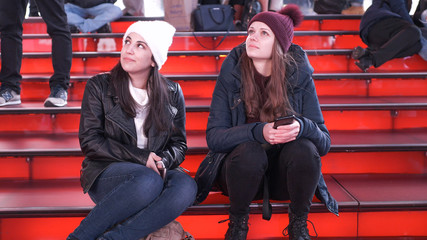 Two girls at Times Square by night sit on the famous red steps