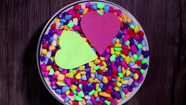 Two multicolored decorative hearts on a background of bright multi-colored pebbles. The concept of Valentine's Day and love.