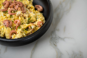 Krabben Rührei mit Friesischen Nordseekrabben und Dill in schwarzer Schale auf Marmor Hintergrund