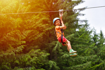 Happy kid with helmet and harness on zip line between trees