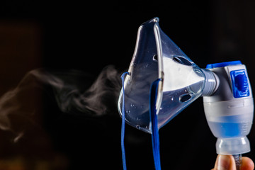 mask nebulizer produces a pair of drugs on a dark background. close-up of face mask - obrazy, fototapety, plakaty