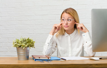 Portrait of young student sitting on her desk doing tasks covering ears with hands, angry and tired of hearing some sound