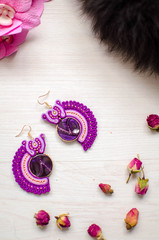 Beaded bracelet and earrings set. Pink and purple soutache jewelry with flowers on the white wooden background. Women accessories