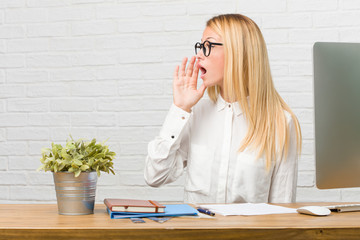 Portrait of young student sitting on her desk doing tasks whispering gossip undertone, trying not...