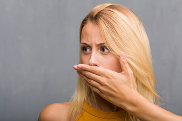 Face closeup, portrait of a natural young blonde woman covering mouth, symbol of silence and repression, trying not to say anything