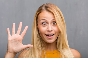 Face closeup, portrait of a natural young blonde woman showing number five, symbol of counting, concept of mathematics, confident and cheerful